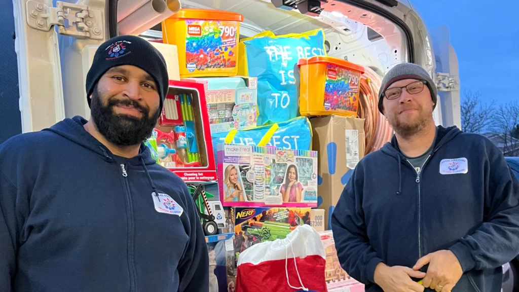 Two smiling employees of Total Aire Care in branded attire standing in front of their service van with its door open, showcasing an array of colorful home care products.