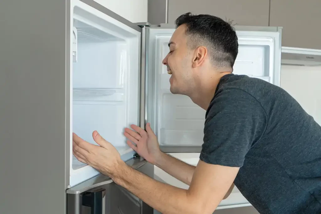 Man cooling off by standing in front of an open refrigerator, indicating a need for air conditioning solutions or relief from heat.