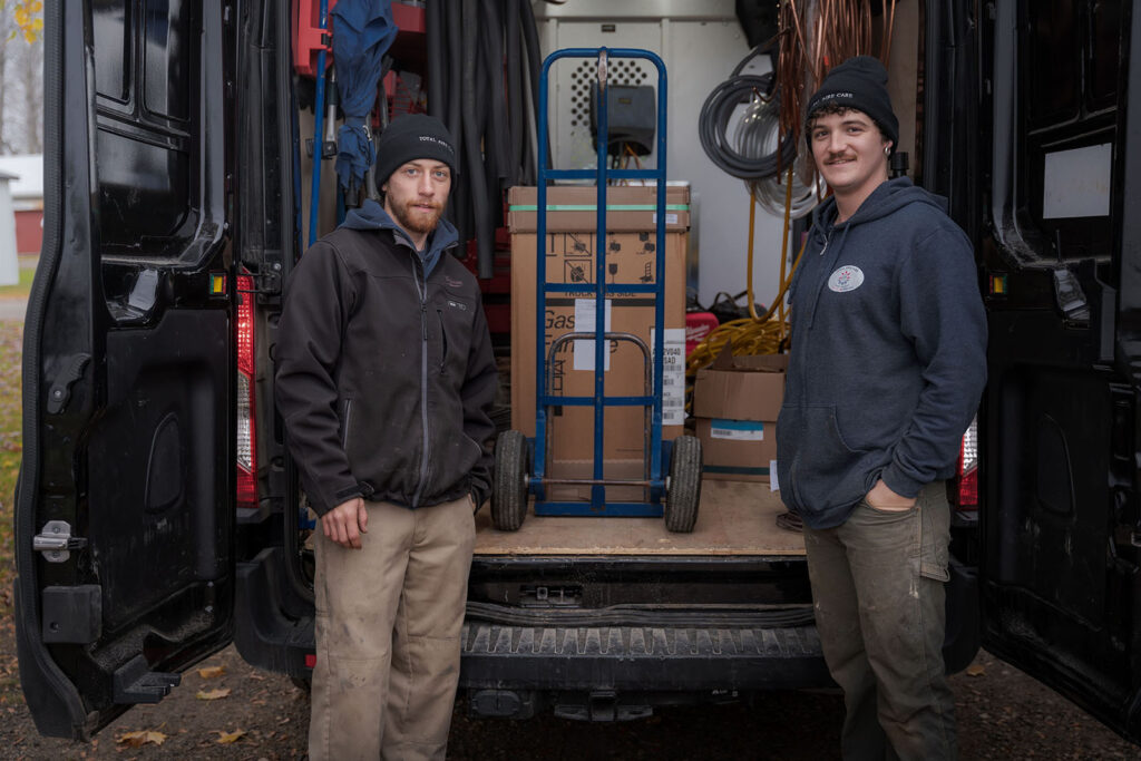 Two technicians from Total Aire Care standing by a service van, equipped with a dolly and boxes, potentially providing services under the Canada Greener Homes Grant program.