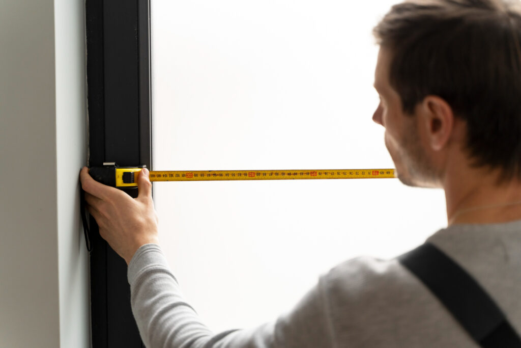 Maintenance worker precisely measuring a window frame with a yellow tape measure, illustrating professional home improvement and accurate service.