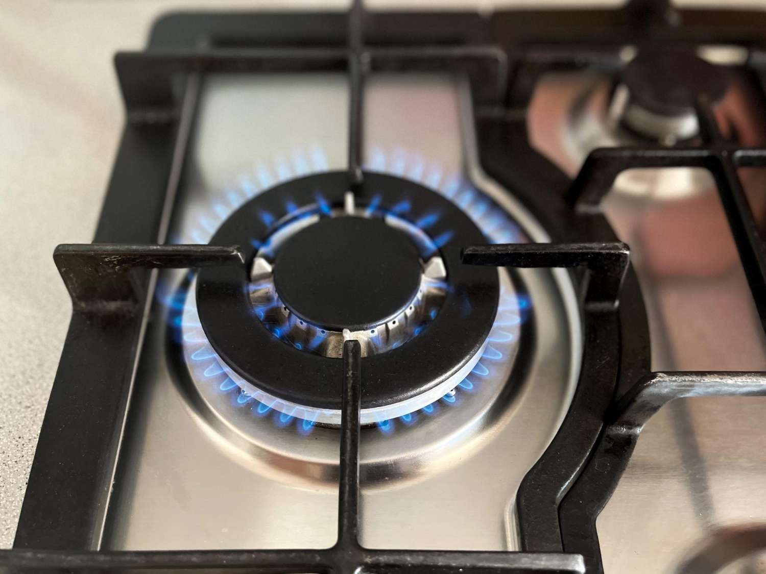 "Close-up of a lit gas stove burner with blue flames, showcasing the burner's metal grates and reflective stainless steel surface, emphasizing the need for gas lines for stoves