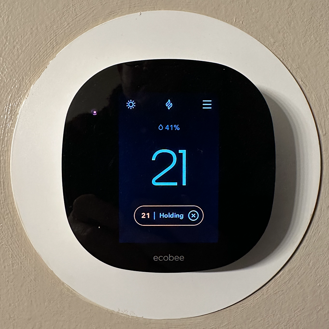 Ecobee smart thermostat displaying 21 degrees Celsius on the wall, indicating active temperature holding.